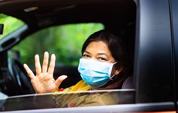 Photo of senior wearing face covering while waving from a car