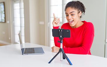 Photo of young adult woman using mobile phone, computer and speaker for virtual presentation